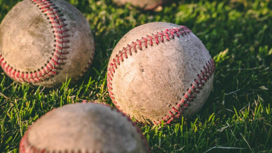 close up photography of four baseballs on green lawn grasses