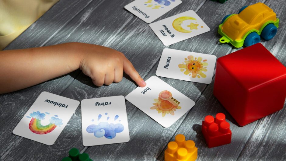 close up of a child pointing at a card lying on a table with toys