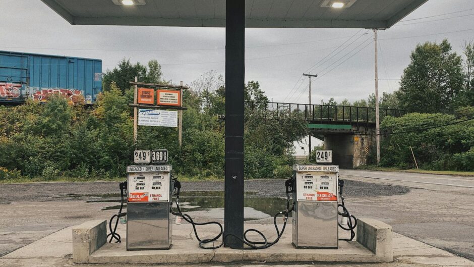 An outdoor scene of an abandoned gas station with dual pumps and vivid greenery in the background.