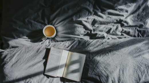 white ceramic mug beside book on gray textile